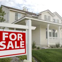 white home with a large front porch and a green front lawn with a for sale sign in front of it