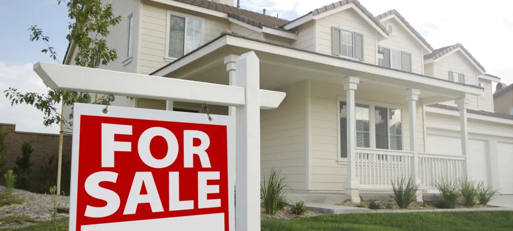 white home with a large front porch and a green front lawn with a for sale sign in front of it