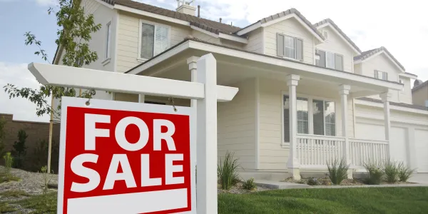 white home with a large front porch and a green front lawn with a for sale sign in front of it